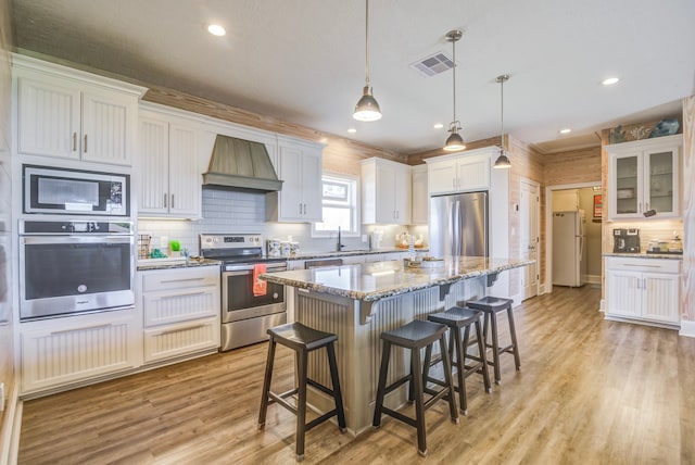 kitchen with stainless steel appliances, a center island, pendant lighting, and white cabinets