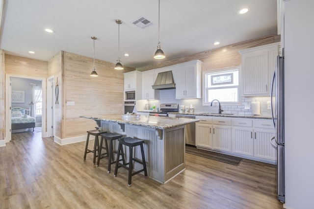 kitchen featuring premium range hood, visible vents, white cabinets, a center island, and pendant lighting