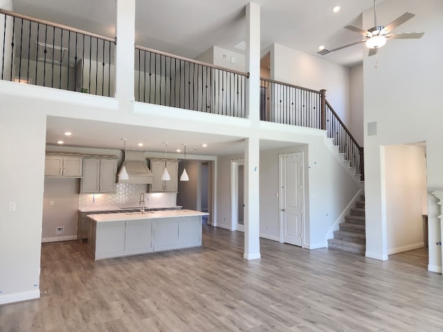 kitchen featuring ceiling fan, decorative light fixtures, a center island with sink, a high ceiling, and light hardwood / wood-style floors