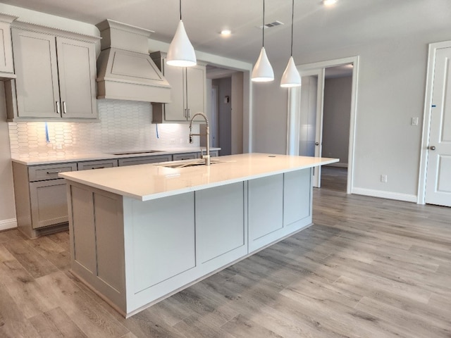 kitchen with gray cabinetry, pendant lighting, a center island with sink, light hardwood / wood-style flooring, and custom range hood