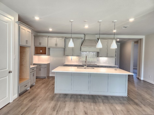 kitchen featuring sink, light hardwood / wood-style flooring, decorative light fixtures, a center island with sink, and custom exhaust hood