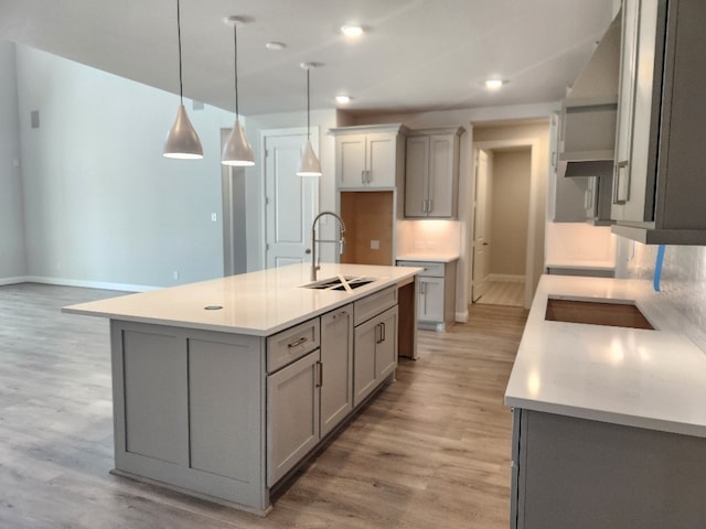 kitchen featuring gray cabinetry, sink, pendant lighting, a center island with sink, and light hardwood / wood-style floors