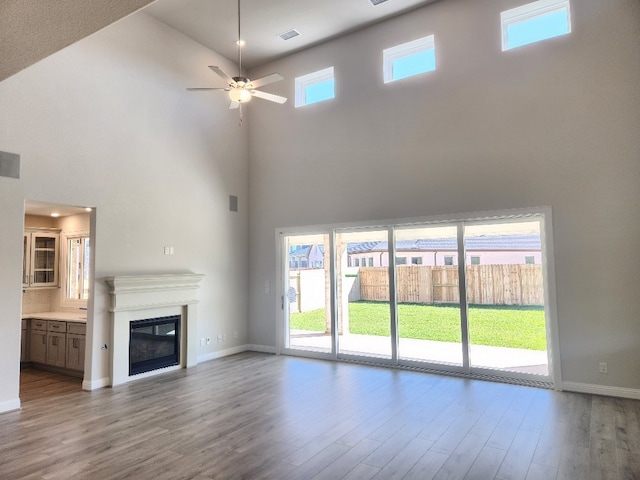 unfurnished living room featuring a high ceiling, light hardwood / wood-style flooring, and ceiling fan