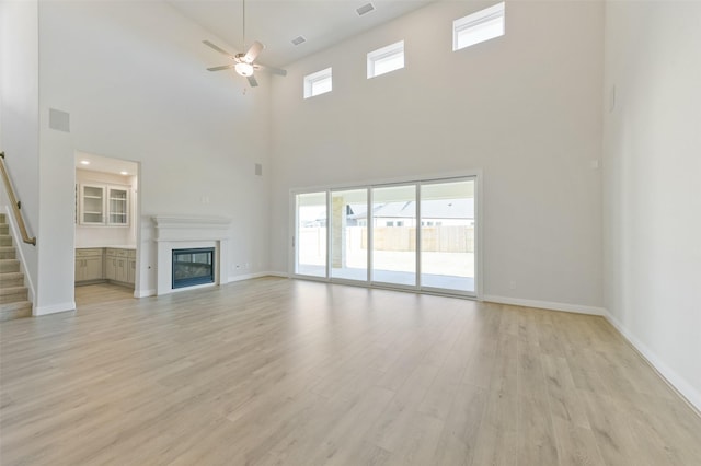 unfurnished living room featuring ceiling fan, a wealth of natural light, light hardwood / wood-style flooring, and a high ceiling