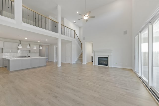 unfurnished living room featuring a high ceiling, ceiling fan, and light hardwood / wood-style flooring