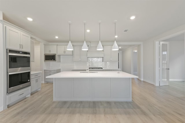 kitchen with pendant lighting, a center island with sink, custom exhaust hood, and appliances with stainless steel finishes