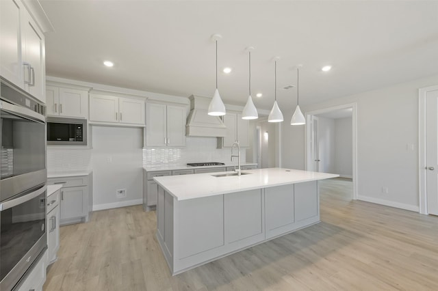 kitchen featuring built in microwave, sink, decorative light fixtures, custom range hood, and a kitchen island with sink