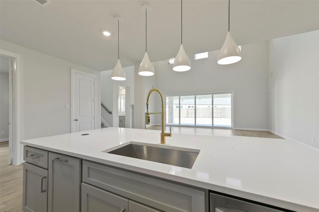 kitchen with gray cabinets, sink, hanging light fixtures, and light wood-type flooring