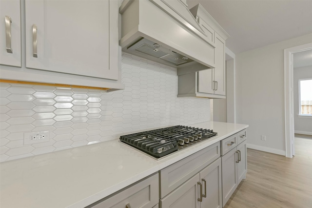 kitchen with light hardwood / wood-style flooring, tasteful backsplash, light stone counters, stainless steel gas cooktop, and custom exhaust hood