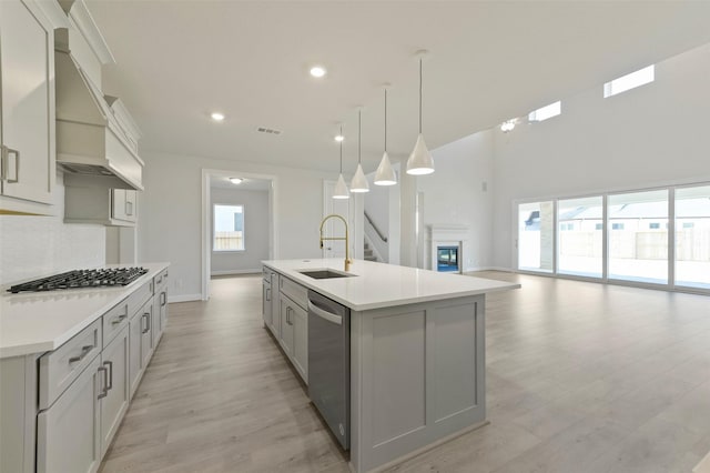 kitchen featuring pendant lighting, sink, gray cabinets, stainless steel appliances, and a center island with sink