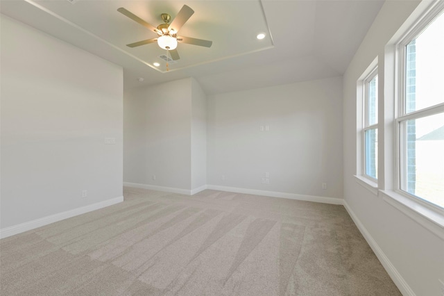 spare room with ceiling fan, a tray ceiling, and light carpet