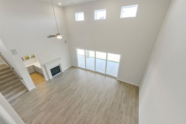 unfurnished living room featuring light hardwood / wood-style floors, ceiling fan, and a high ceiling