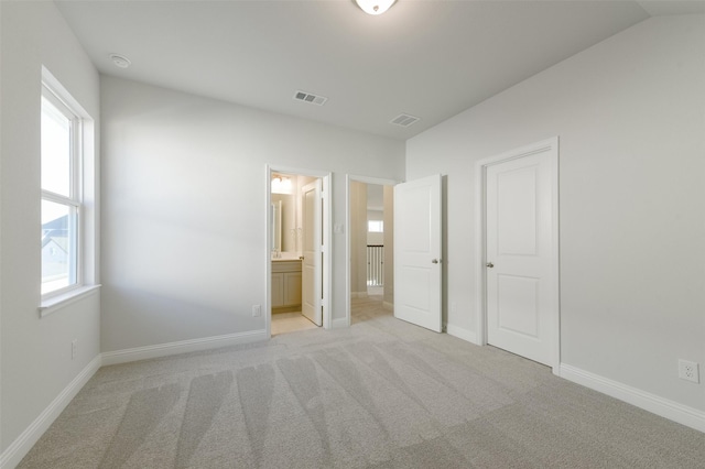 unfurnished bedroom with vaulted ceiling, ensuite bath, light colored carpet, and multiple windows