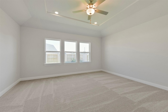 spare room with ceiling fan, lofted ceiling, a tray ceiling, and light carpet