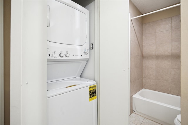 washroom with stacked washer and clothes dryer, light tile patterned floors, and a textured ceiling