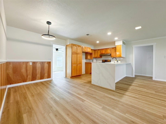 kitchen with hanging light fixtures, kitchen peninsula, sink, ceiling fan, and light wood-type flooring