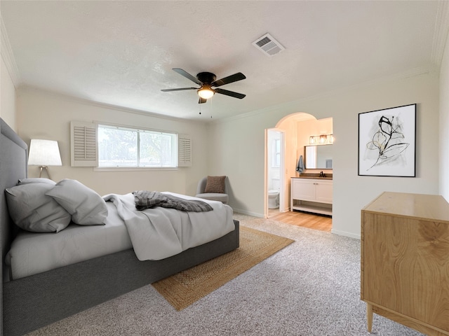 bedroom featuring ceiling fan, light colored carpet, ornamental molding, and ensuite bath