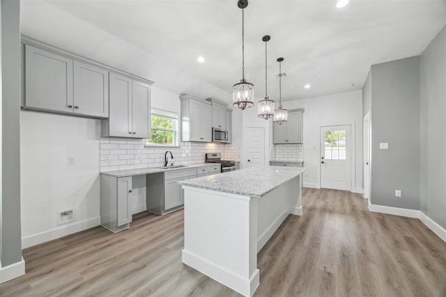 kitchen with light stone counters, sink, a kitchen island, light hardwood / wood-style flooring, and stainless steel appliances