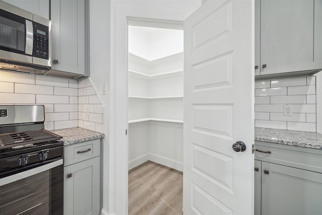 kitchen featuring light stone counters, tasteful backsplash, gray cabinets, stainless steel appliances, and light hardwood / wood-style flooring