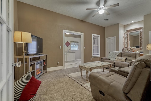 living room featuring a textured ceiling, light colored carpet, sink, and ceiling fan