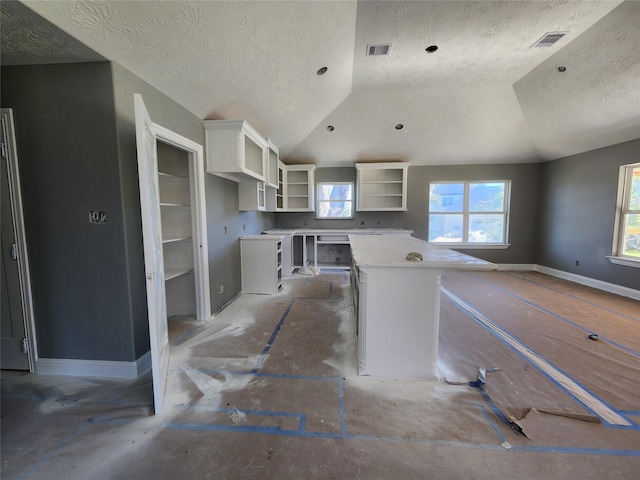 kitchen featuring a textured ceiling, white cabinets, a kitchen island, and lofted ceiling