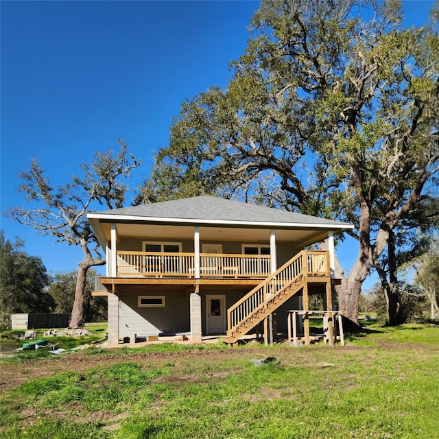 rear view of property featuring a deck, roof with shingles, stairway, and a lawn