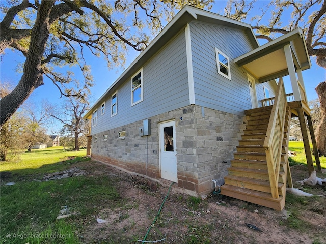 rear view of house featuring stone siding, a lawn, and stairs