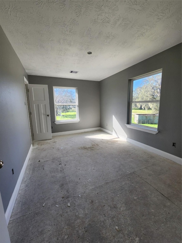 unfurnished room with visible vents, a textured ceiling, and baseboards