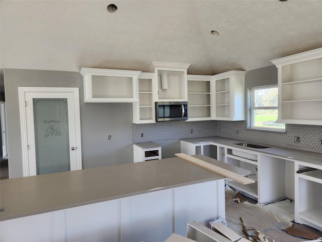 kitchen featuring white cabinets, stainless steel microwave, decorative backsplash, and open shelves