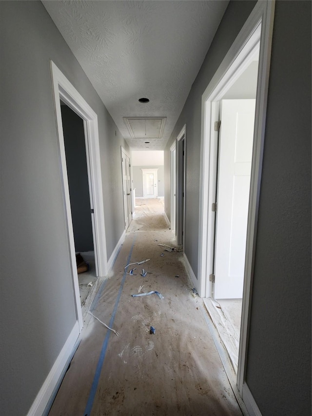 hall with attic access, a textured ceiling, and baseboards