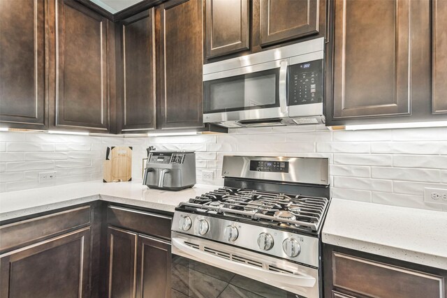 kitchen with appliances with stainless steel finishes, dark brown cabinets, light stone counters, and backsplash