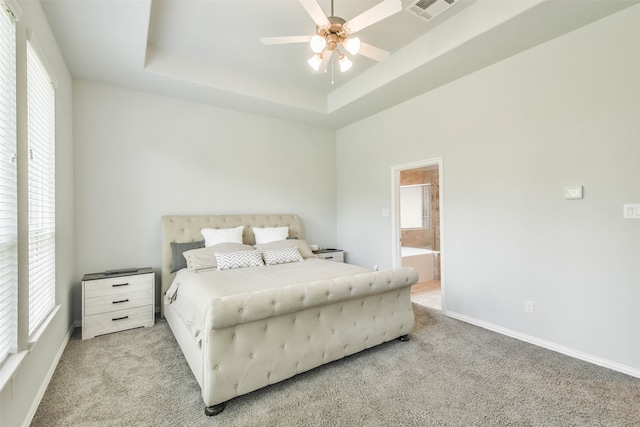 carpeted bedroom with ensuite bath, ceiling fan, and a tray ceiling