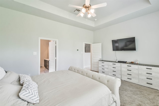 bedroom featuring light carpet, connected bathroom, ceiling fan, and a tray ceiling