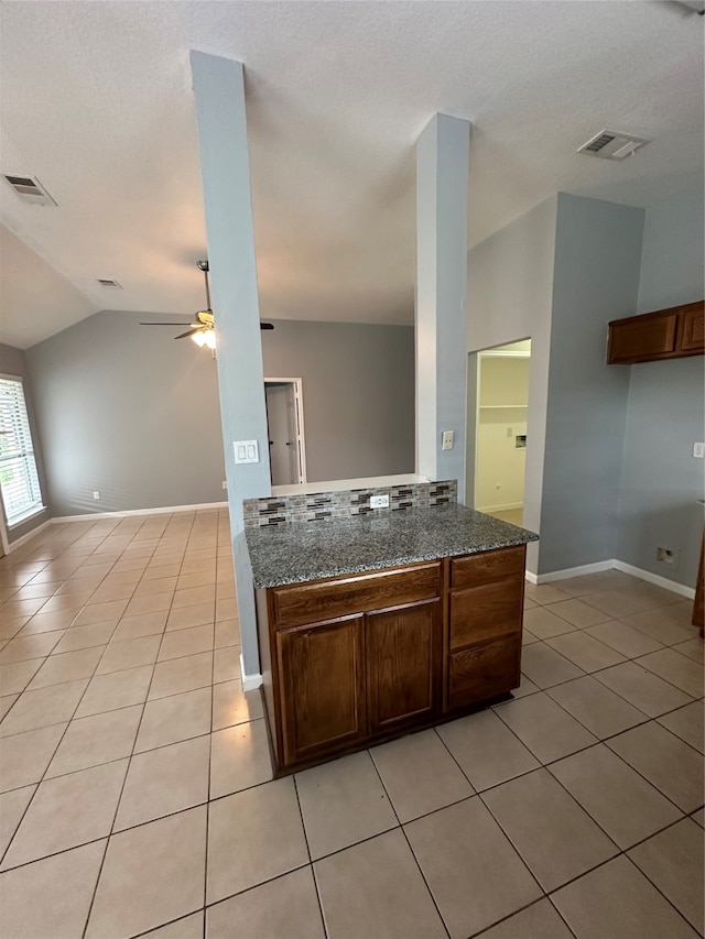 kitchen featuring dark stone counters, light tile patterned floors, ceiling fan, lofted ceiling, and kitchen peninsula