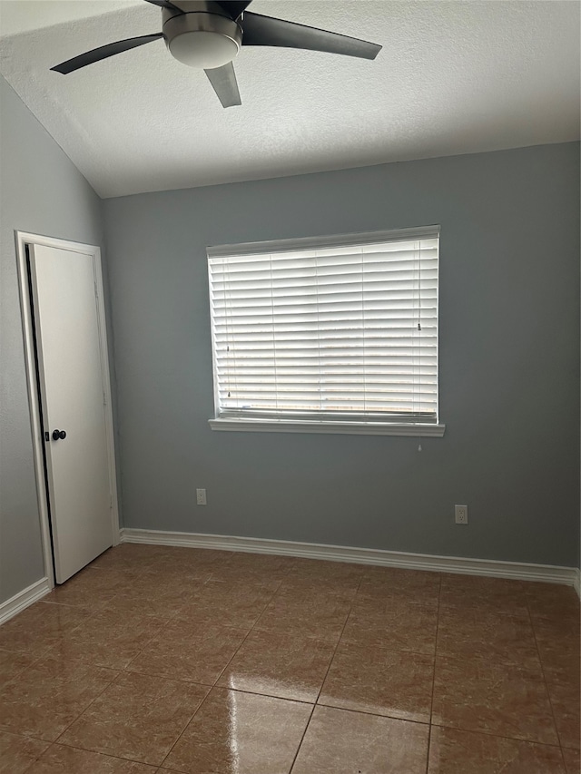 tiled spare room featuring a textured ceiling, lofted ceiling, and ceiling fan