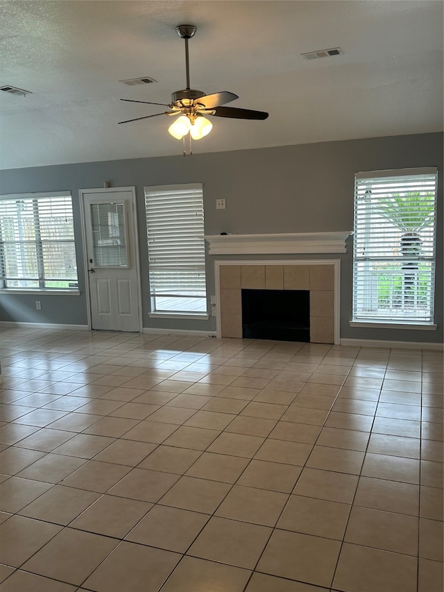 unfurnished living room featuring a tiled fireplace, light tile patterned floors, and ceiling fan