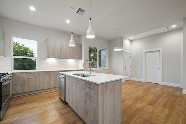 kitchen featuring an island with sink, sink, appliances with stainless steel finishes, light hardwood / wood-style flooring, and backsplash