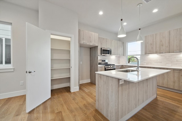 kitchen with sink, appliances with stainless steel finishes, light hardwood / wood-style flooring, and a kitchen island with sink