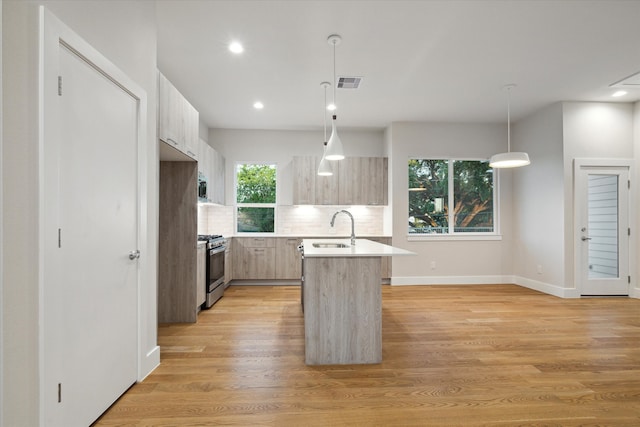 kitchen featuring appliances with stainless steel finishes, tasteful backsplash, light wood-type flooring, and a kitchen island with sink