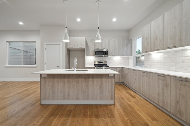 kitchen with stainless steel appliances, light hardwood / wood-style flooring, sink, and an island with sink