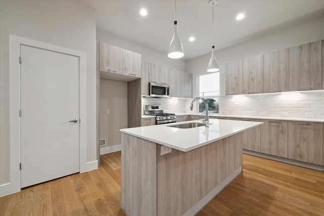 kitchen with light hardwood / wood-style floors, appliances with stainless steel finishes, backsplash, and an island with sink