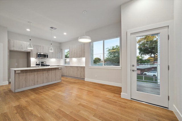 kitchen with light hardwood / wood-style flooring, pendant lighting, decorative backsplash, a kitchen island with sink, and light brown cabinetry