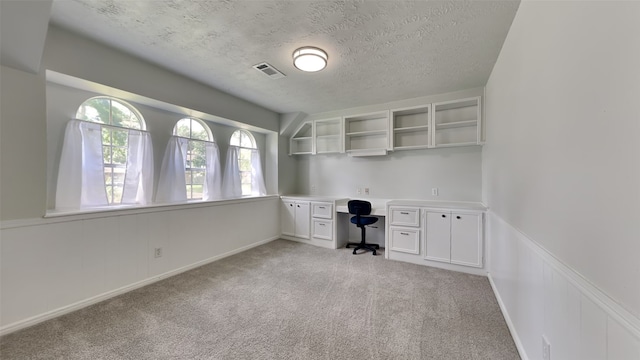 unfurnished office with light carpet, a textured ceiling, and built in desk