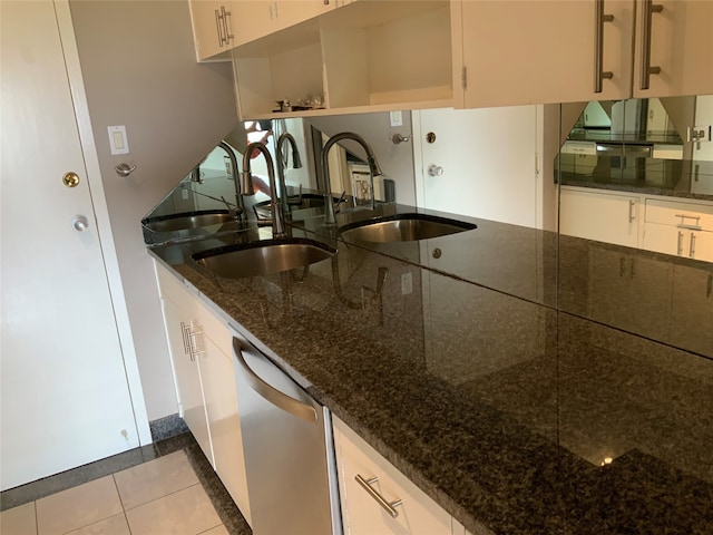 kitchen with dishwasher, sink, light tile patterned flooring, dark stone countertops, and white cabinetry