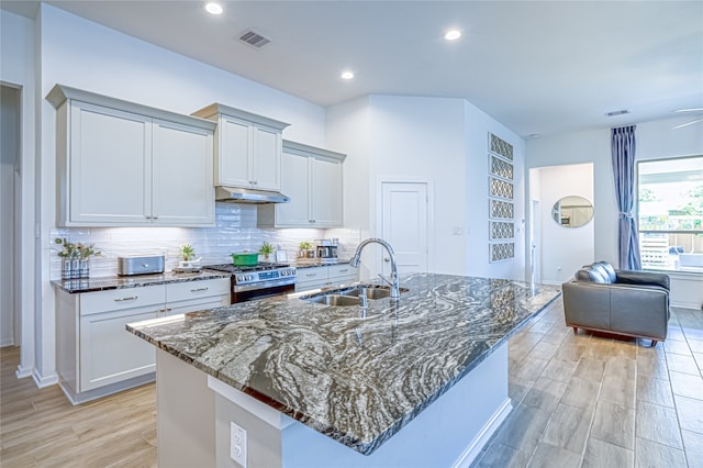 kitchen featuring sink, a kitchen island with sink, backsplash, and gas range