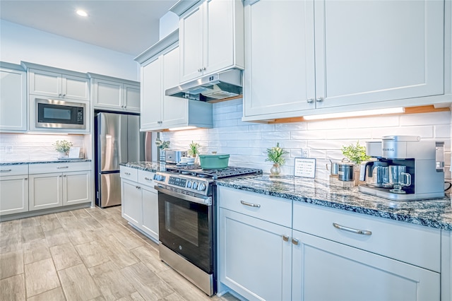 kitchen featuring appliances with stainless steel finishes, dark stone counters, light hardwood / wood-style flooring, and backsplash