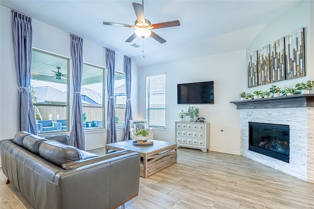 living room featuring a stone fireplace, vaulted ceiling, light wood-type flooring, and ceiling fan