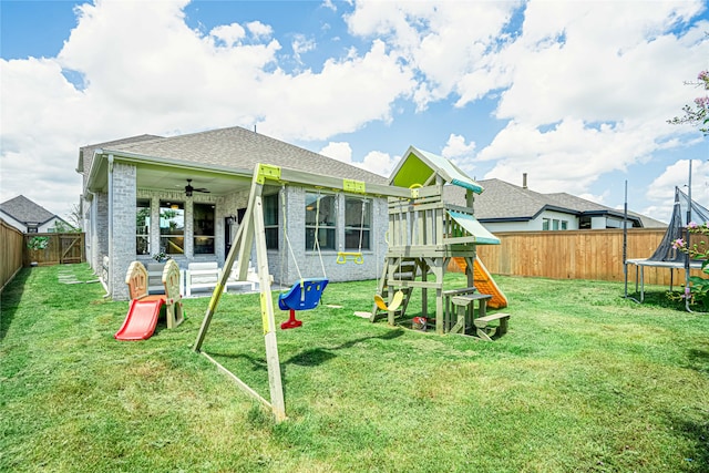 rear view of property featuring ceiling fan, a yard, a trampoline, and a playground