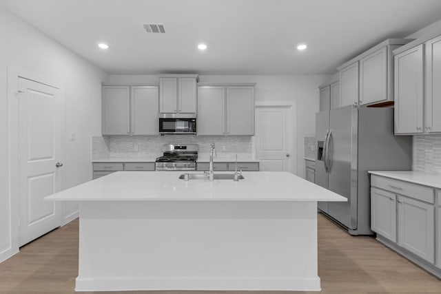 kitchen featuring light wood-type flooring, a center island with sink, gray cabinetry, sink, and appliances with stainless steel finishes