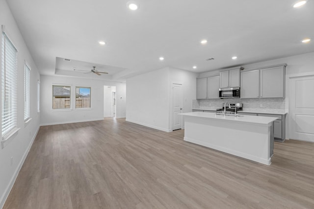 kitchen with gray cabinets, light hardwood / wood-style floors, a kitchen island with sink, and decorative backsplash